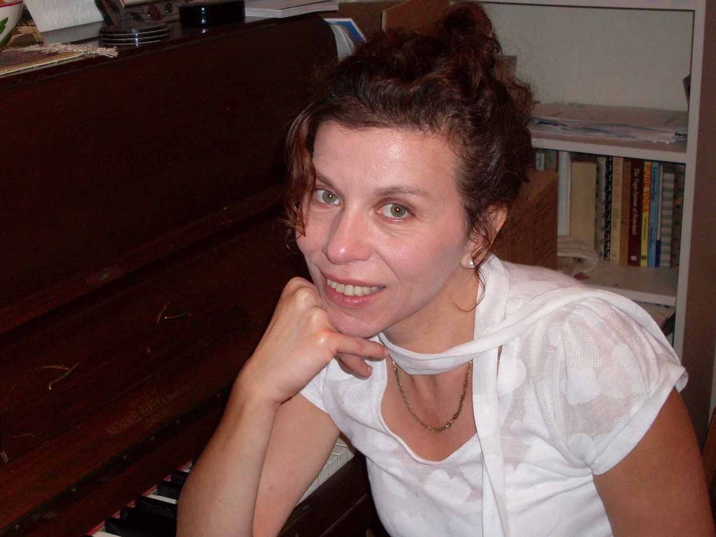 A woman in a white shirt is sitting in front of a piano