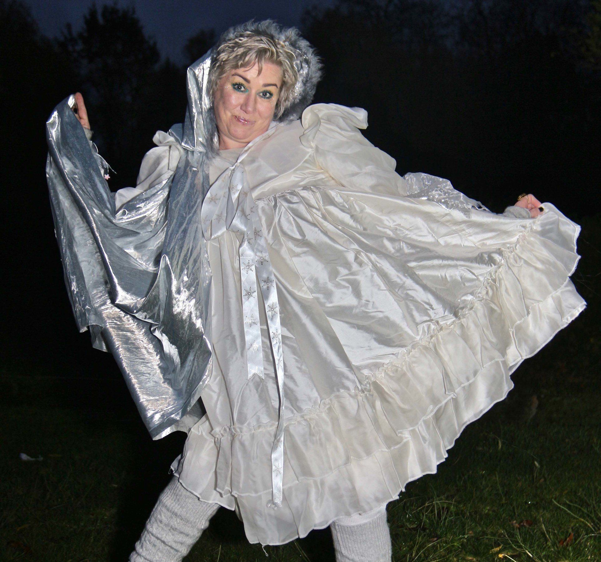 A woman is wearing a white dress and a silver cape