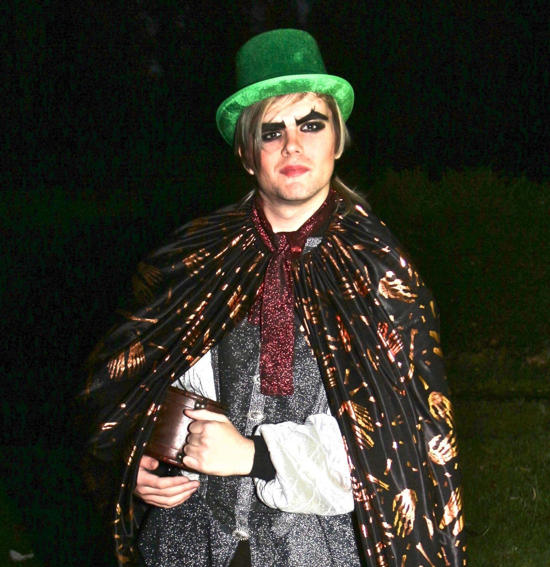 A man wearing a green top hat and a black cape