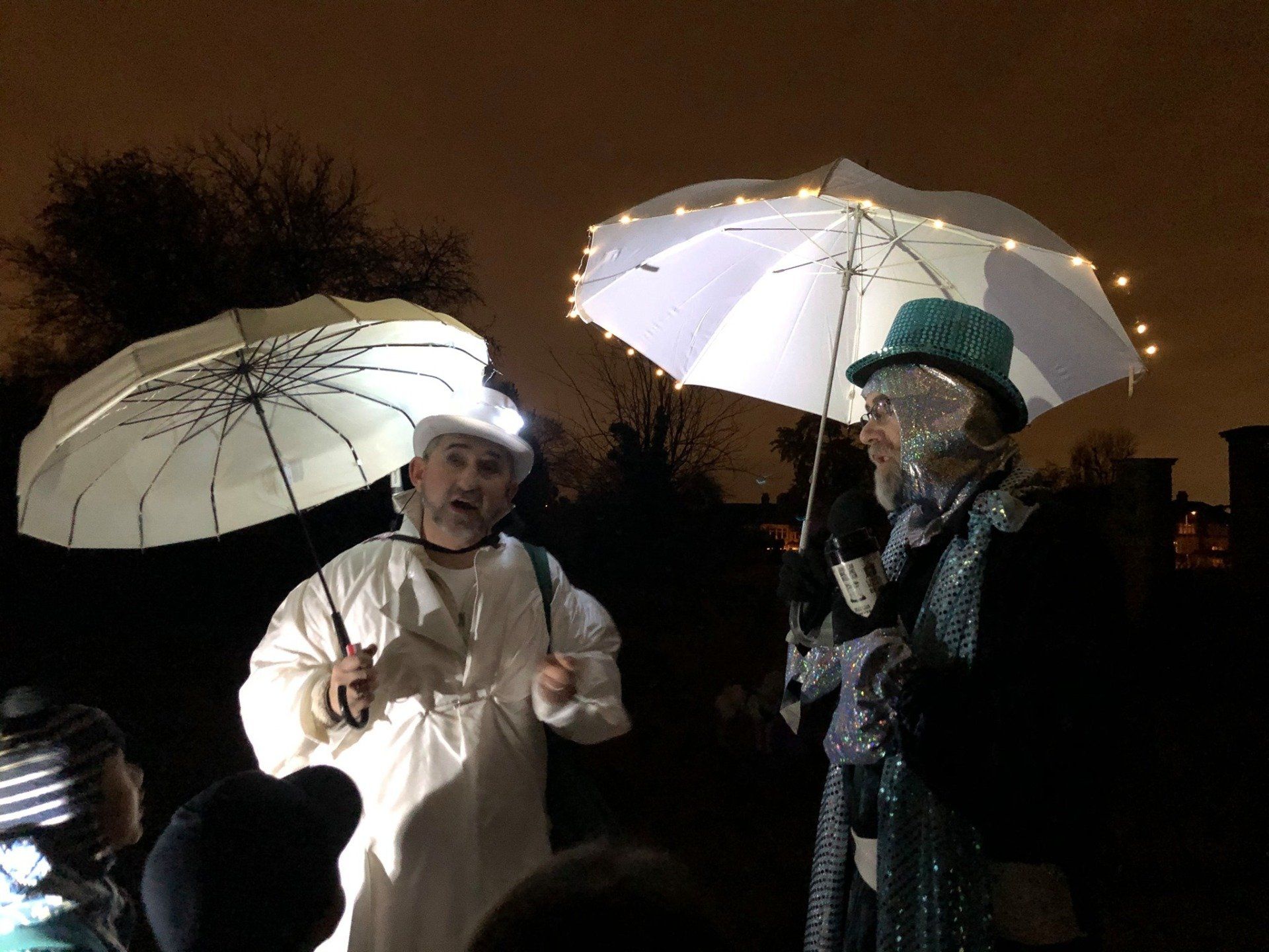 A group of people are standing under umbrellas in the dark.