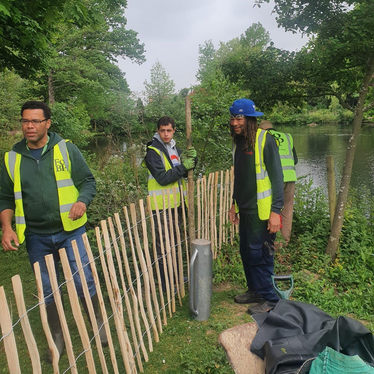Three men in yellow vests are standing next to a wooden fence