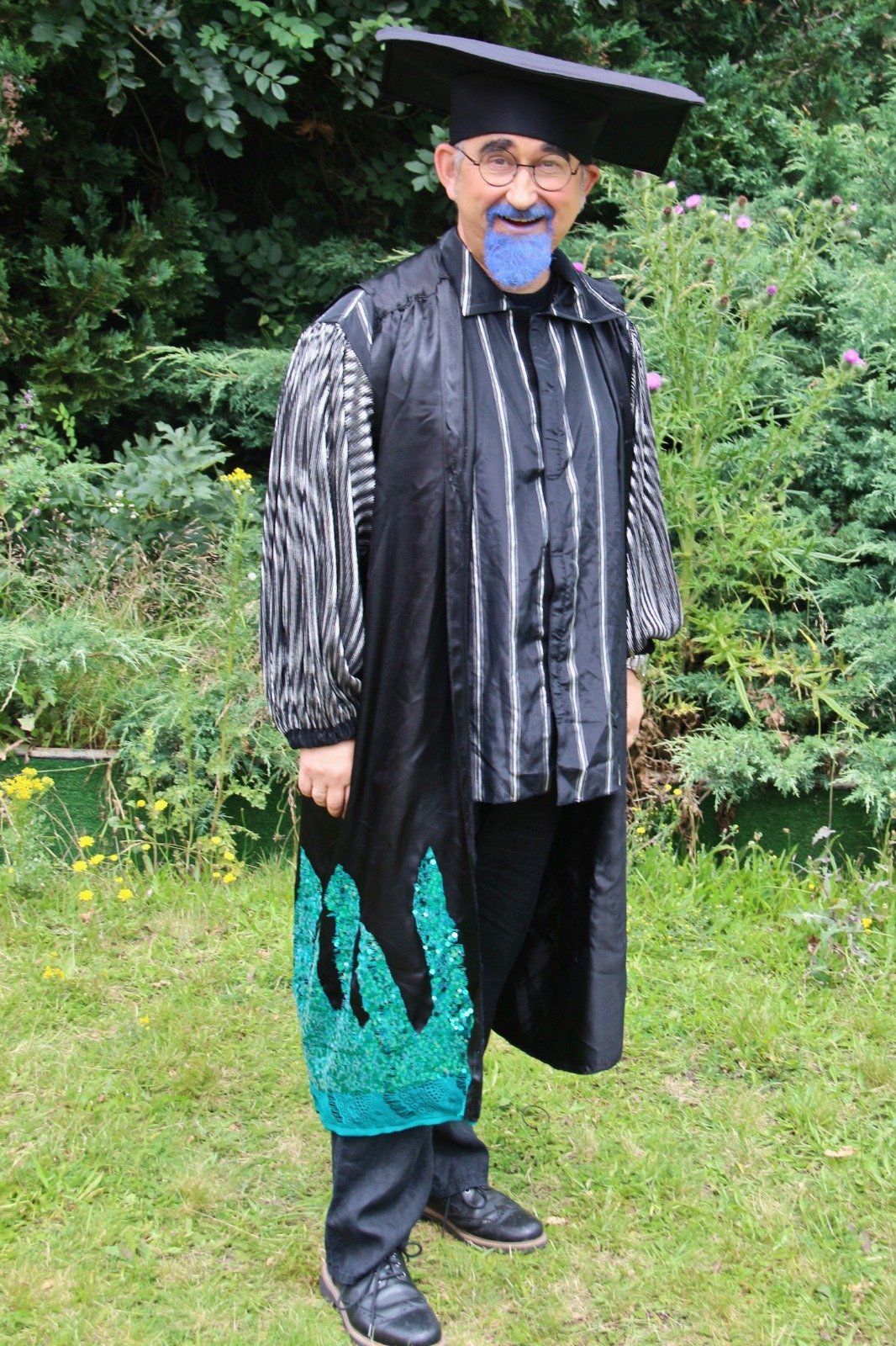 A man wearing a graduation cap and gown is standing in the grass.
