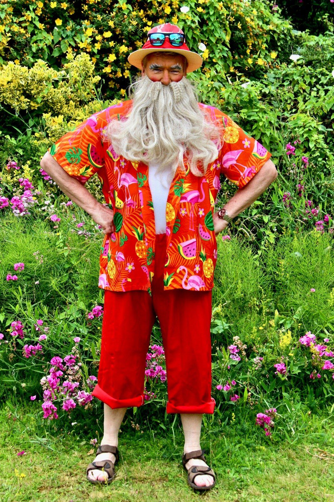 A man with a beard and a hat is standing in a field of flowers.