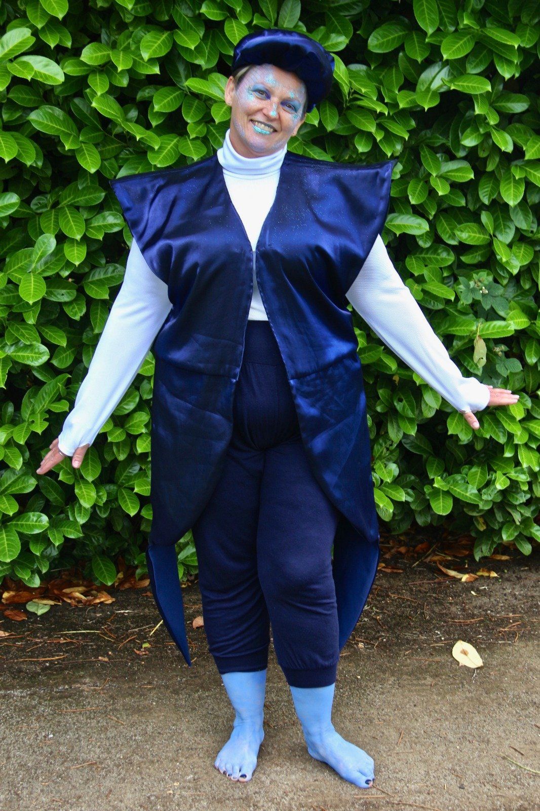 A woman in a blue costume is standing in front of a bush.