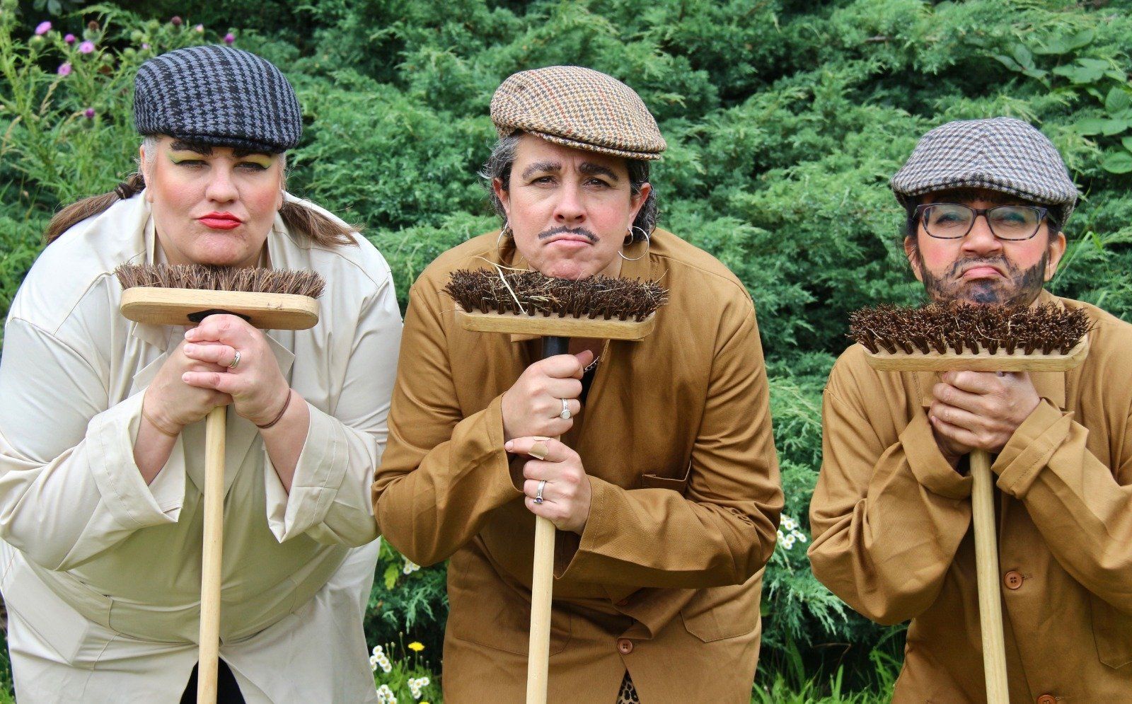 Three people are standing next to each other holding brooms in front of their faces.