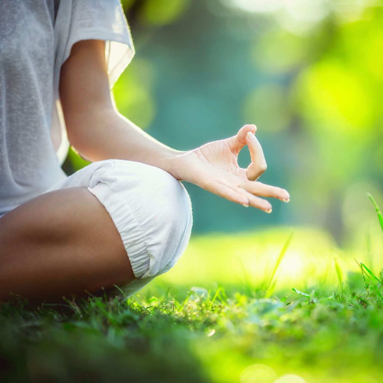 A woman is sitting on the grass in a lotus position.