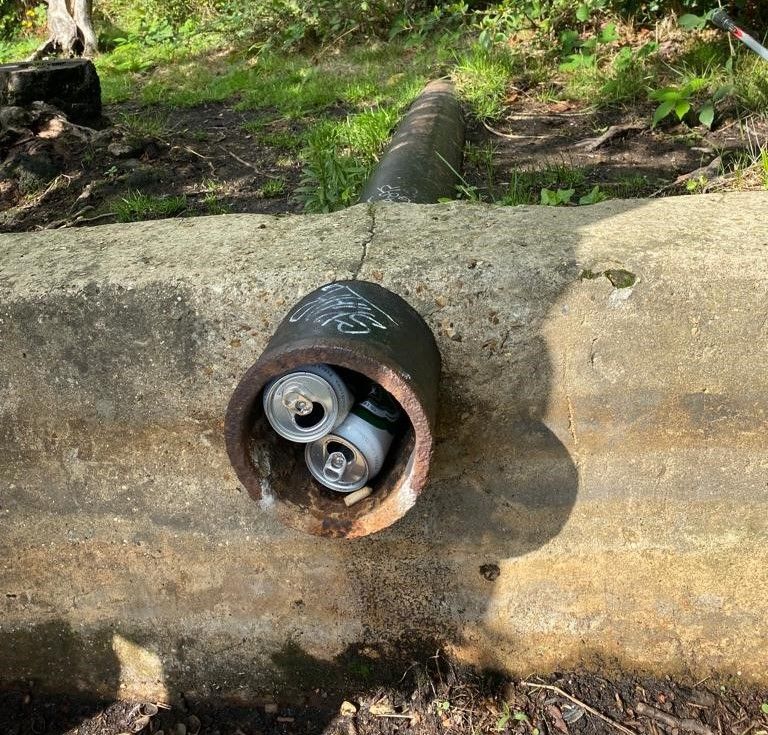Two drinks can are located  in a hole in a pipe.