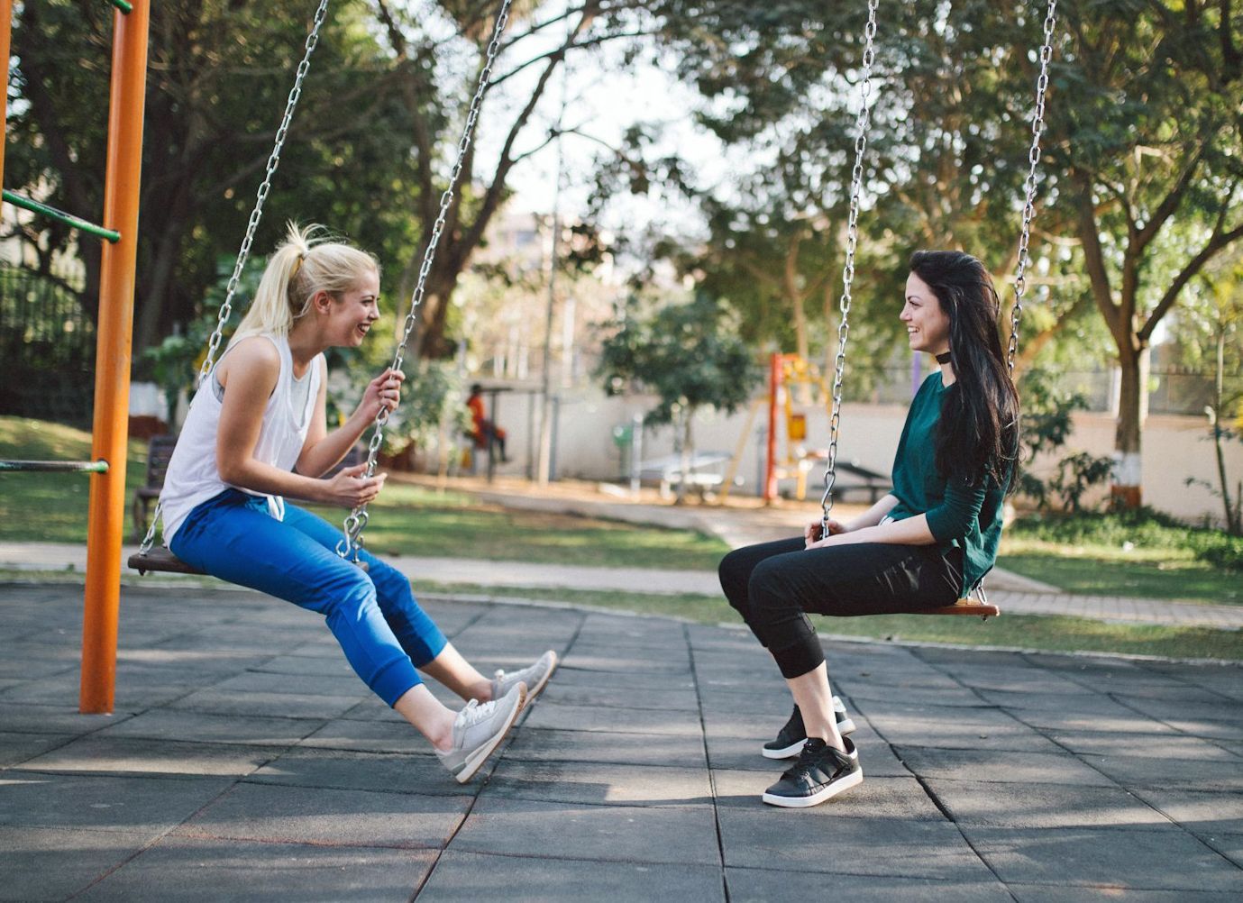 two young women laughing / smiling on swings in the park. 