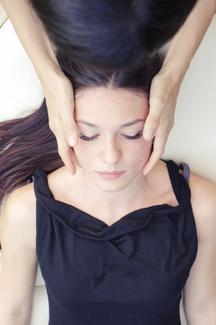 A holistic therapist performs cranial sacral therapy on a young woman.