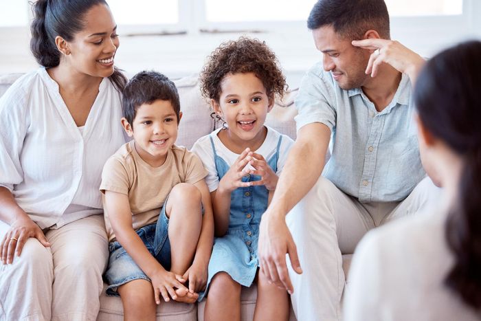 A family is sitting on a couch talking to a woman.