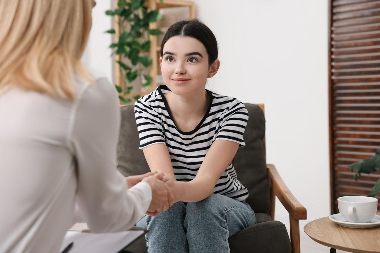 A woman is holding the hand of a young girl while sitting in a chair.