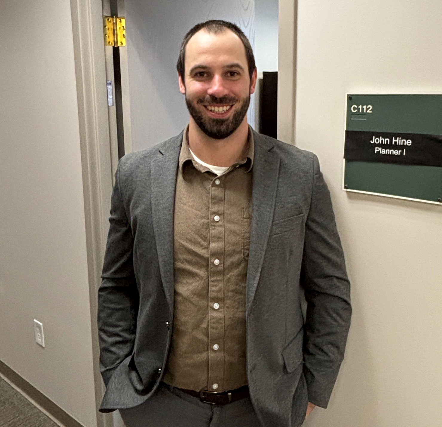 A man in a suit is standing in a hallway next to a sign that says c112