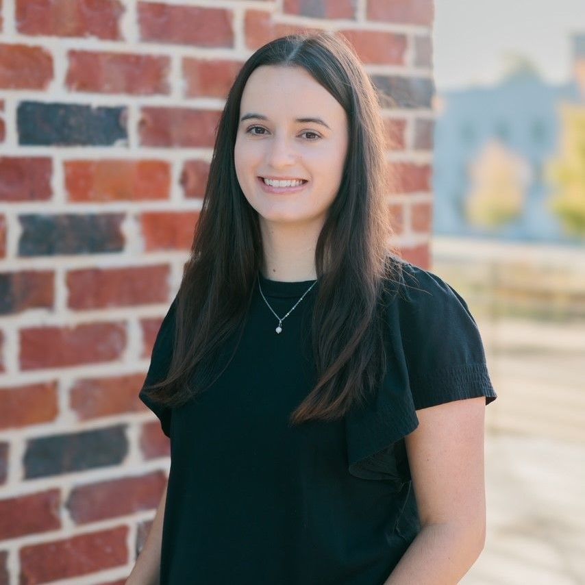 A woman in a black shirt is standing in front of a brick wall.