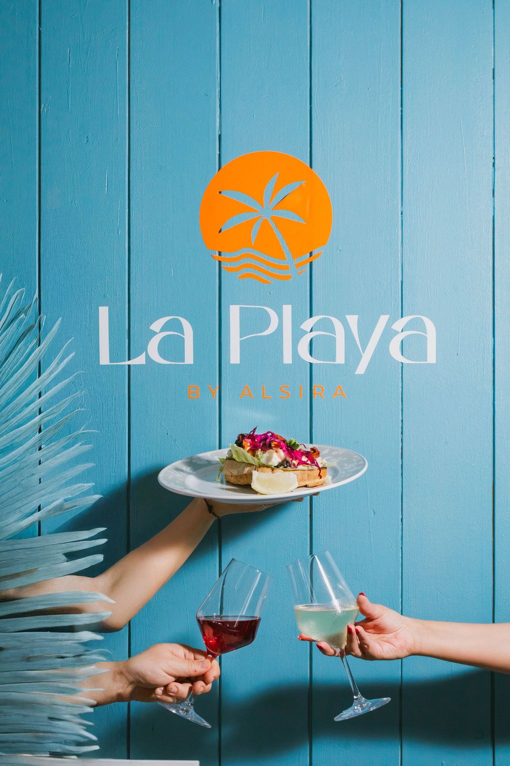 Due persone che tengono bicchieri di vino e un piatto di cibo davanti a un cartello che dice la playa