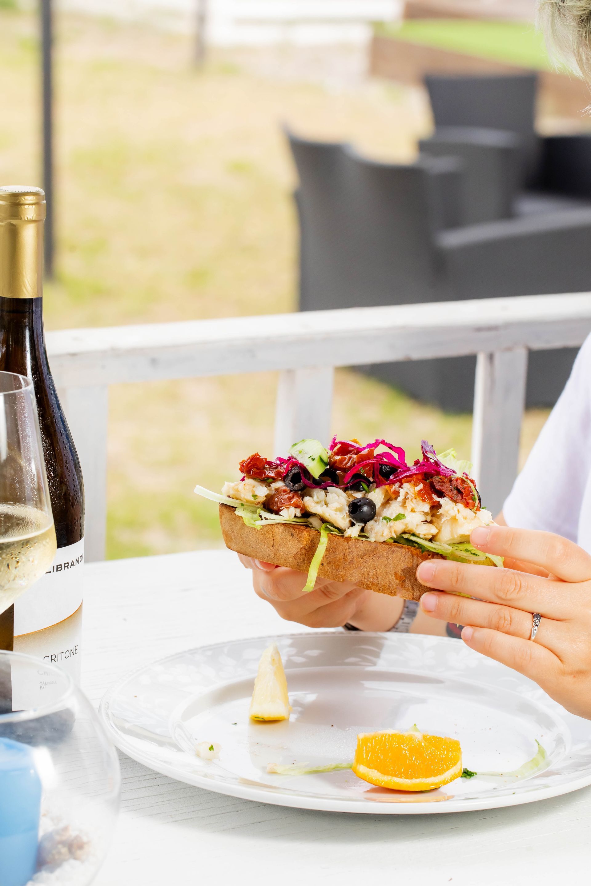 Una persona sta mangiando un panino con una bottiglia di vino sullo sfondo.