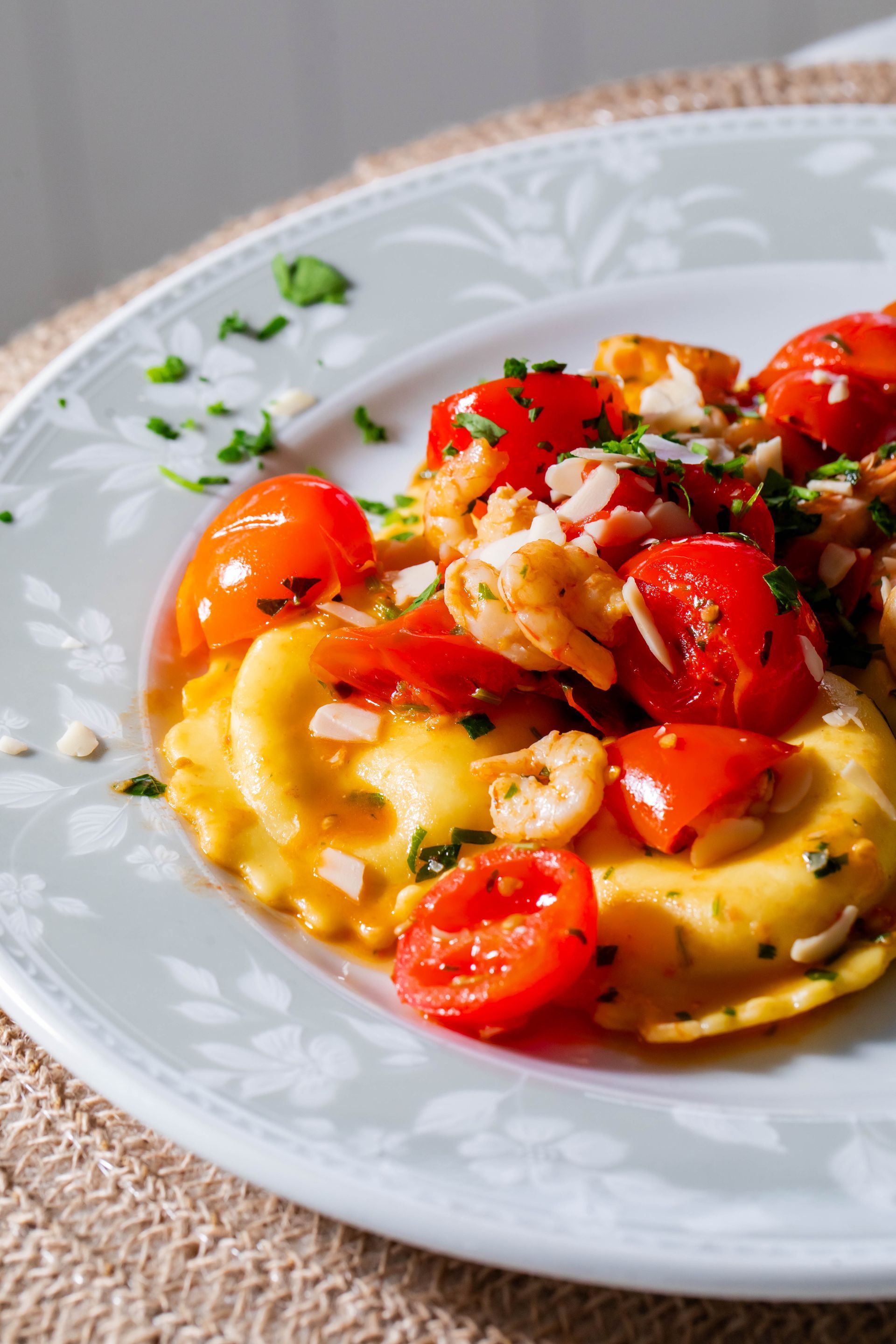 Un piatto bianco con ravioli e pomodori su un tavolo.