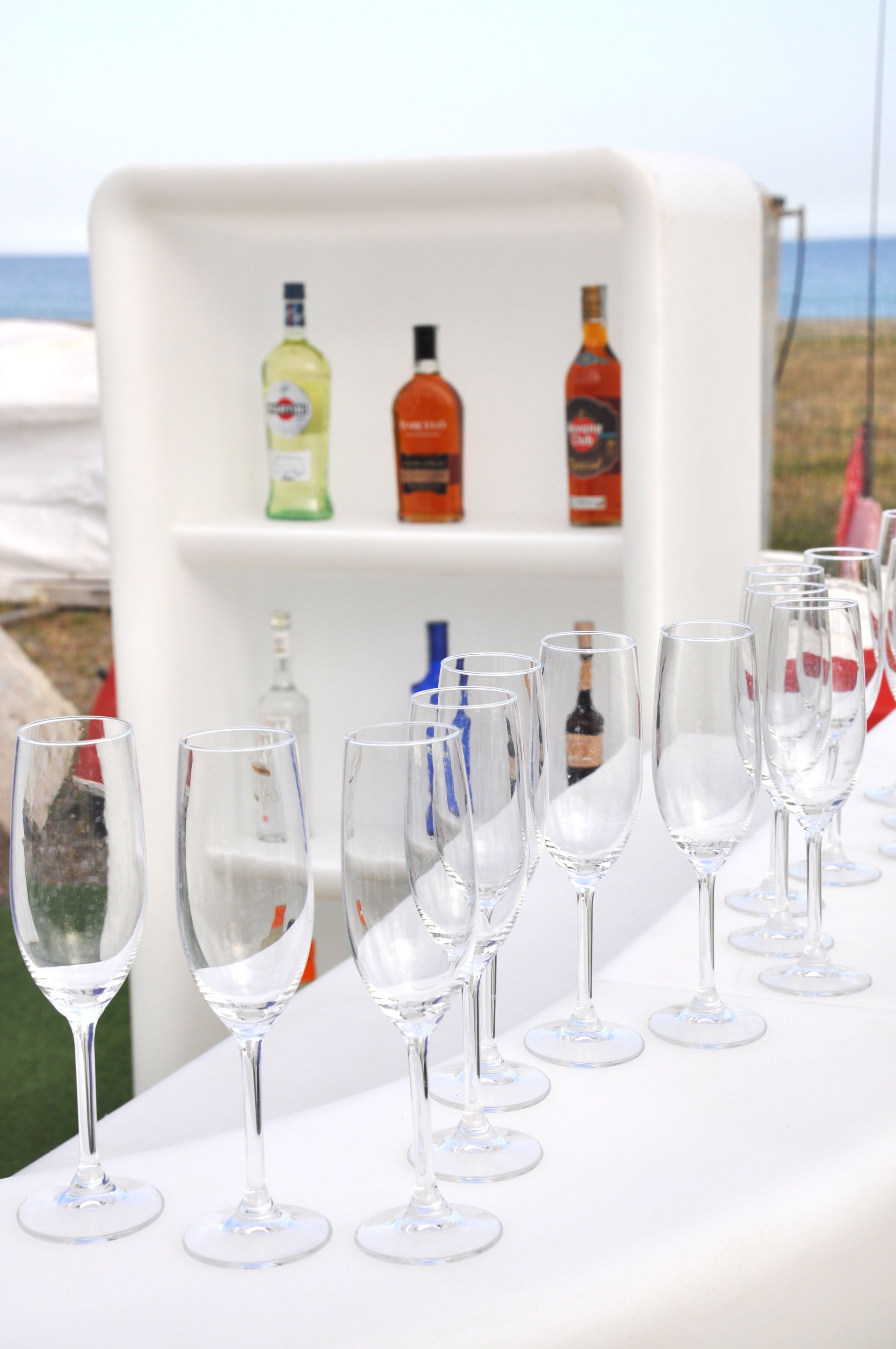 Una fila di bicchieri da vino sono allineati su un tavolo di fronte a uno scaffale con sopra delle bottiglie.