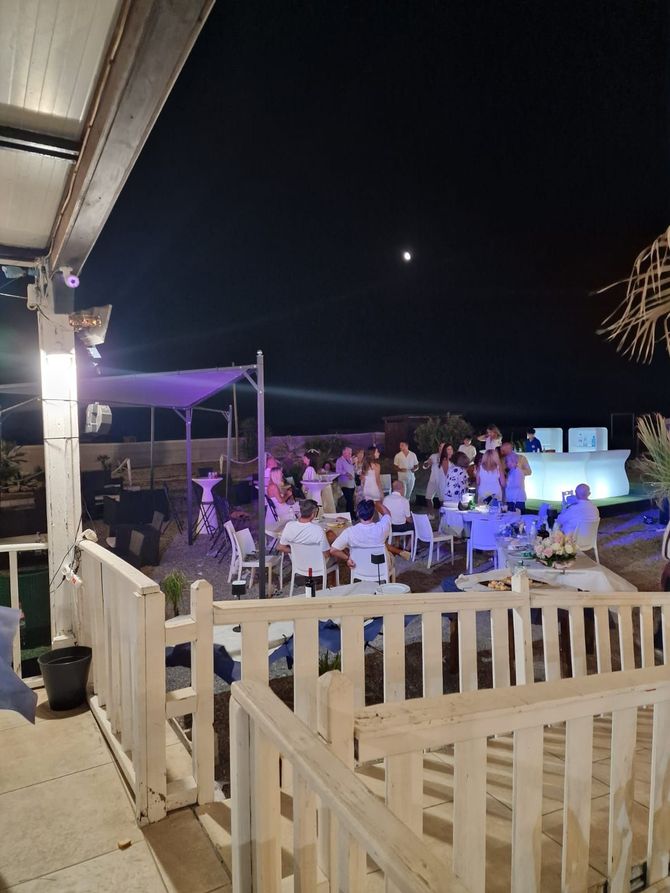 Due persone che tengono bicchieri di vino e un piatto di cibo davanti a un cartello che dice la playa