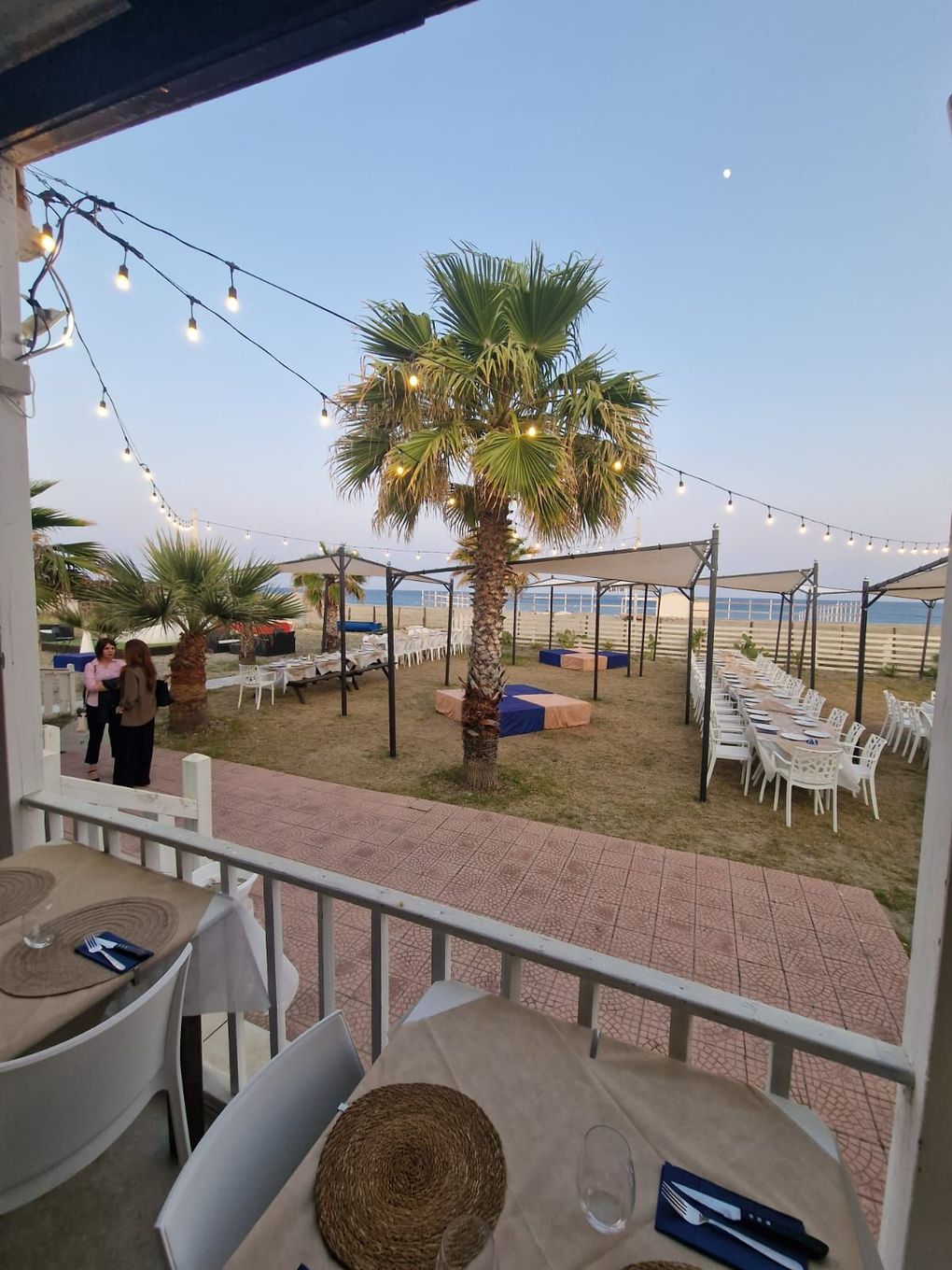 Due persone che tengono bicchieri di vino e un piatto di cibo davanti a un cartello che dice la playa