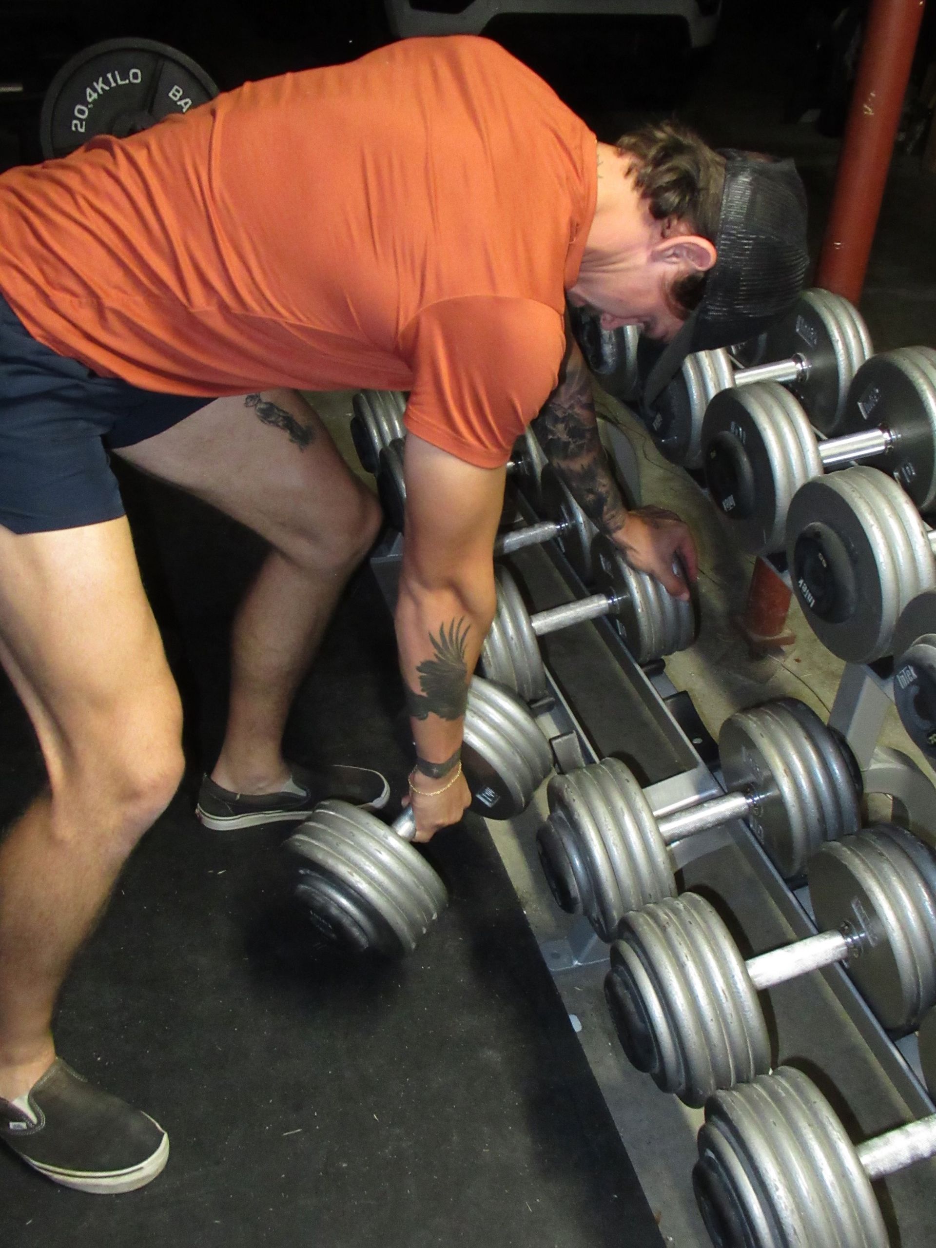 A man in an orange shirt is lifting dumbbells in a gym