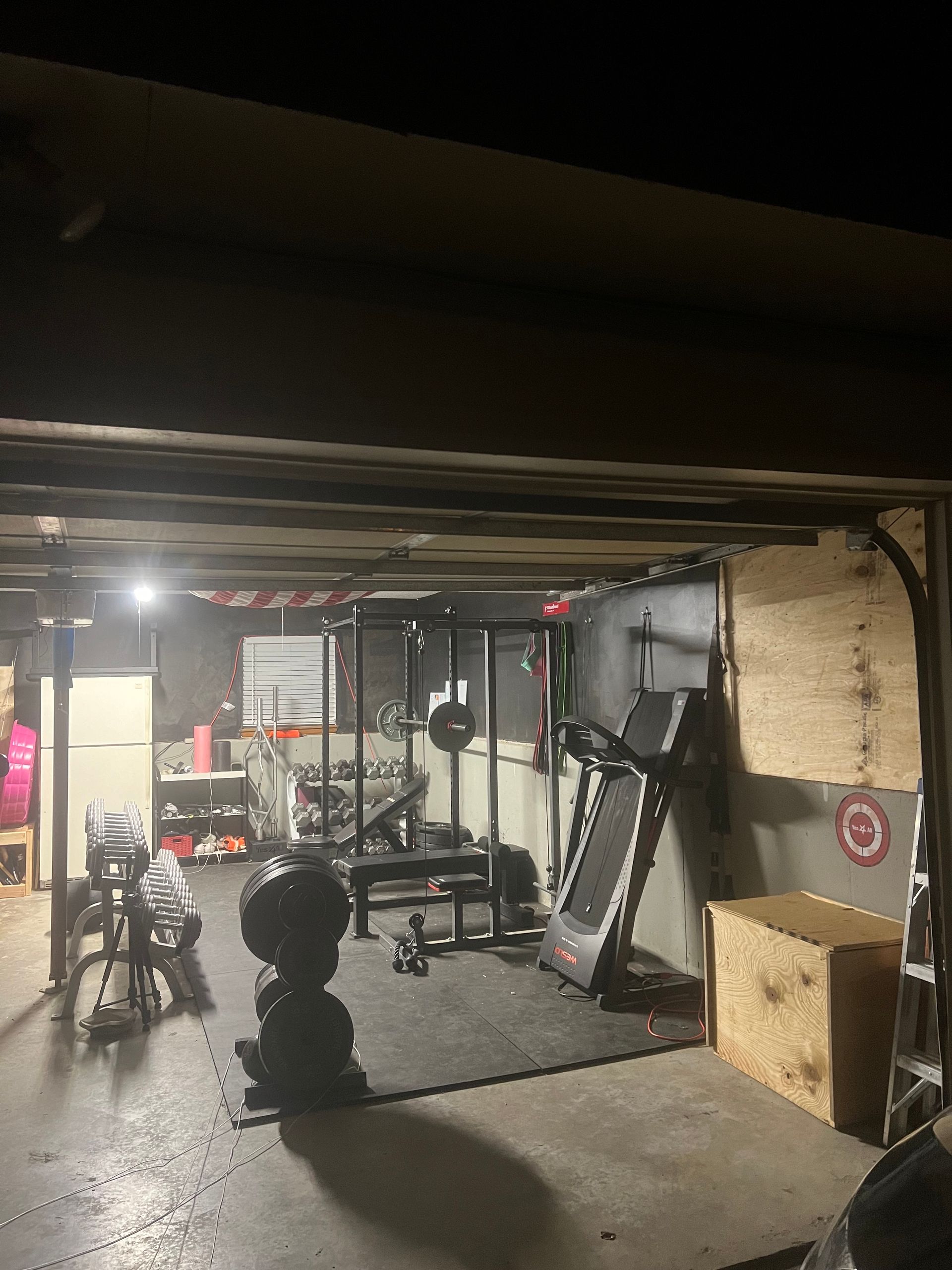 A gym in a garage with a treadmill and a barbell rack.