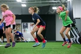 Three young girls are jumping in the air in a gym.