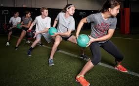 A group of people are doing exercises with medicine balls in a gym.