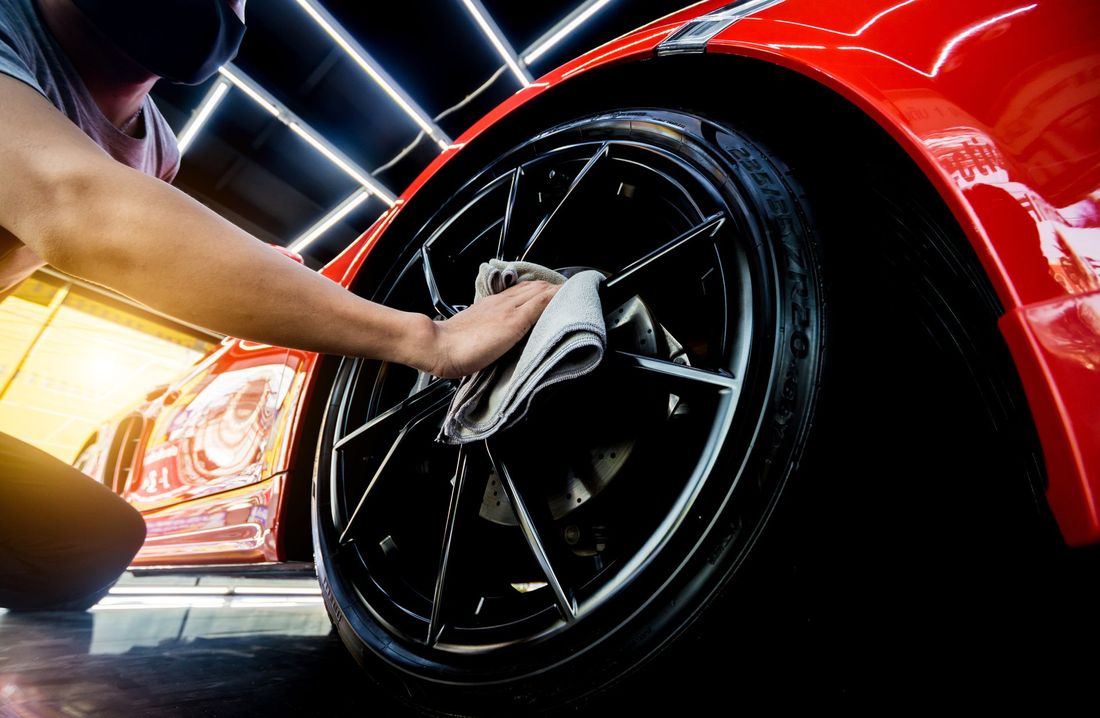 A man is cleaning a car wheel with a towel.