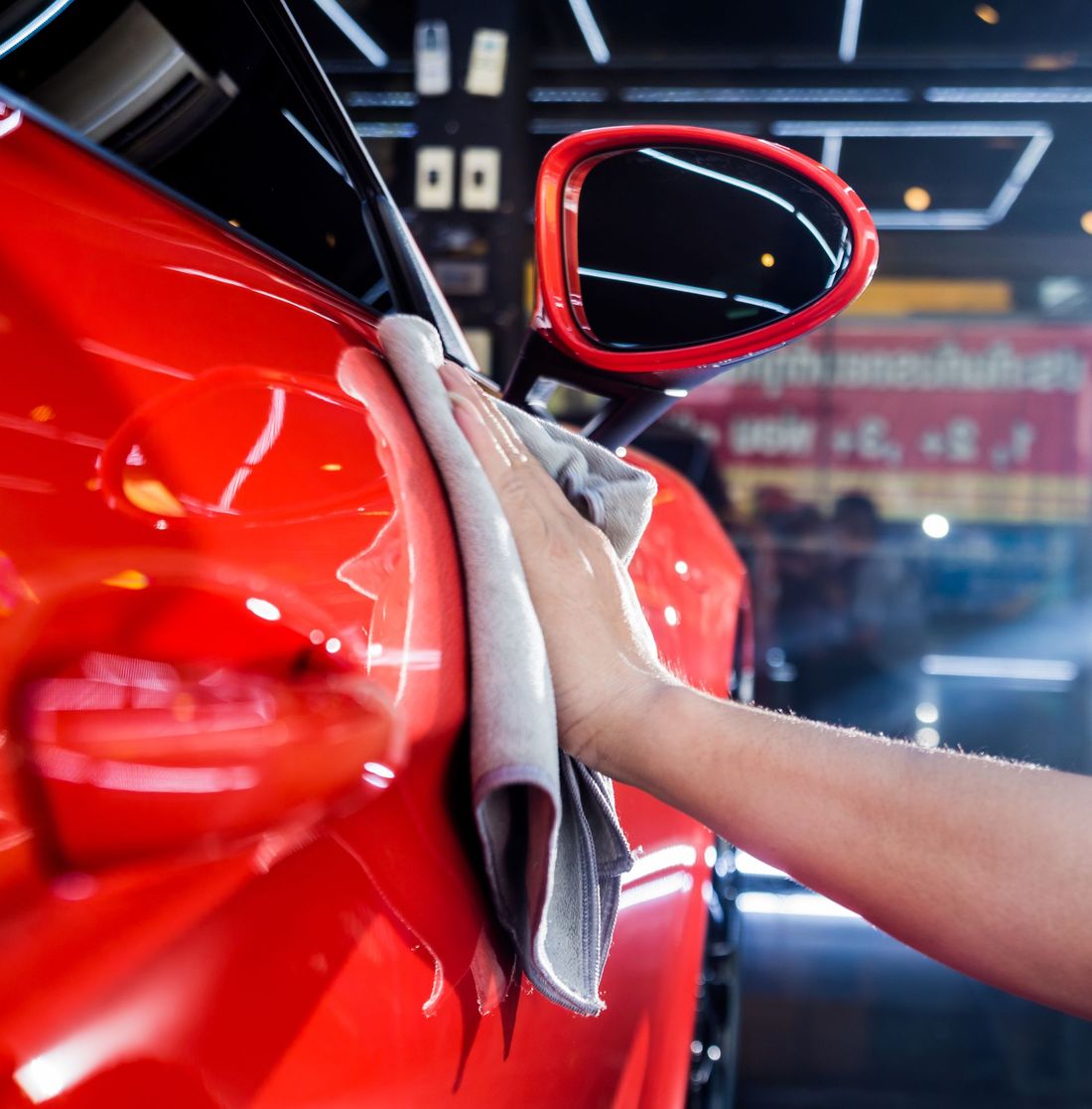 A person is cleaning a red car with a towel