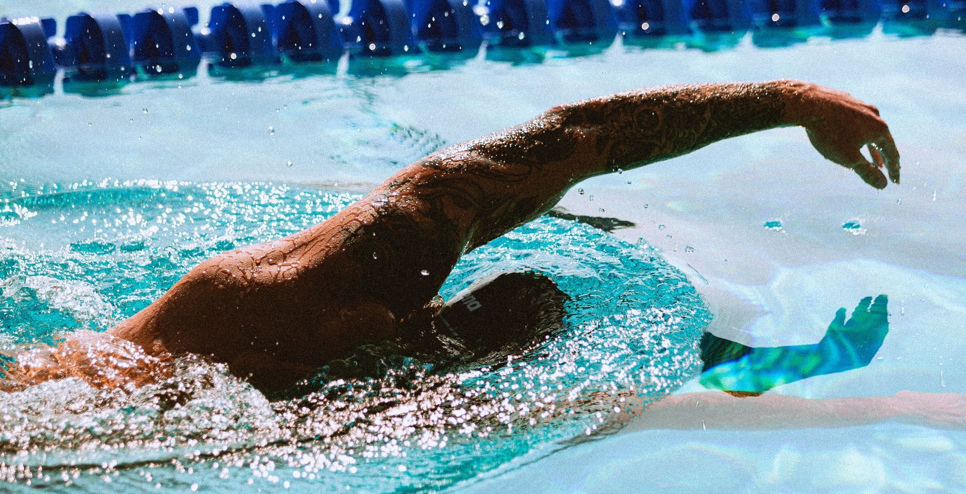 Swimmer's arm reaching forward, pulling through water, in an outdoor pool.