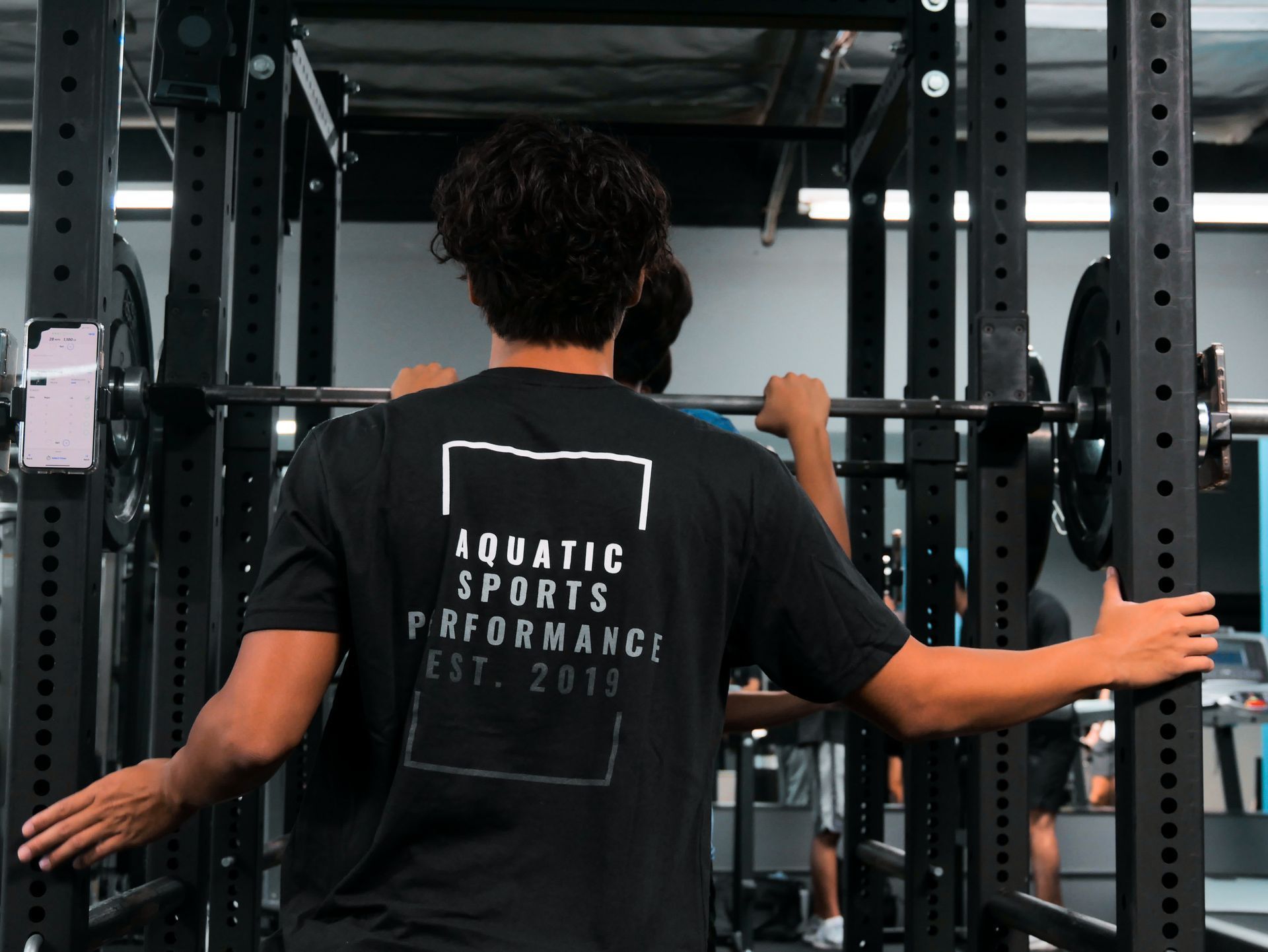 Man in black shirt at a weight rack, grasping the barbell.
