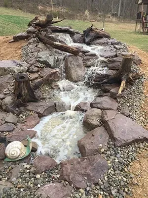 Water cascading down a rocky, man-made waterfall. A snail statue sits near the water's edge.