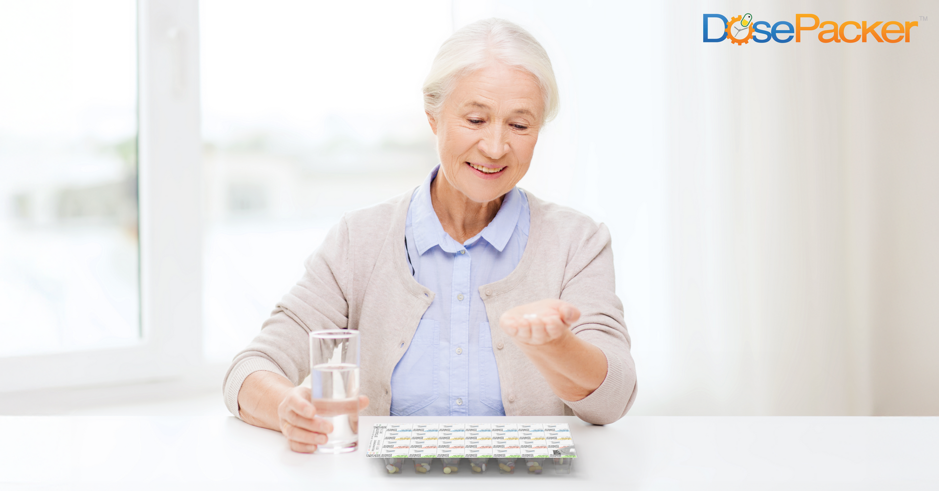 An elderly woman is sitting at a table holding a bottle of pills.