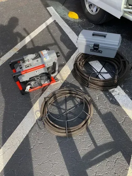 A drain cleaner is sitting on the ground in a parking lot next to a toolbox.