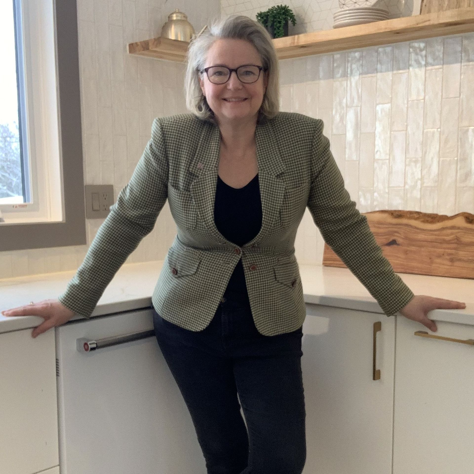 Kawartha Kelli poses in a kitchen, leaning on countertop.