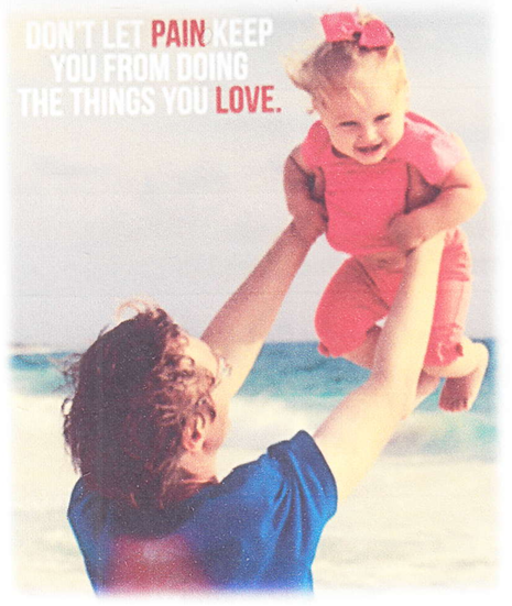 Man holds a smiling child in the air at the beach. Pink outfits, sunny day.
