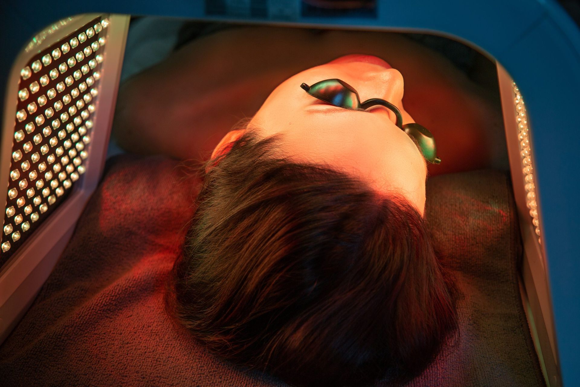 A woman is laying in a bed with red and blue lights on her face.