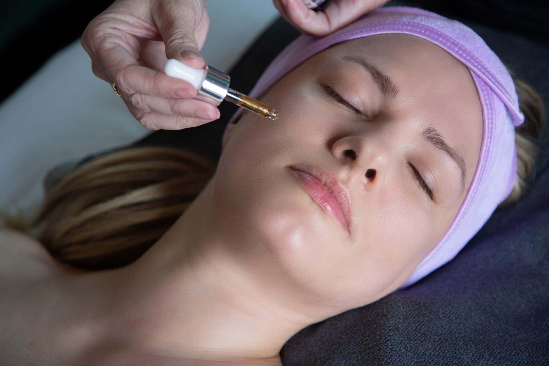 A woman is getting a facial treatment with a pipette on her face.