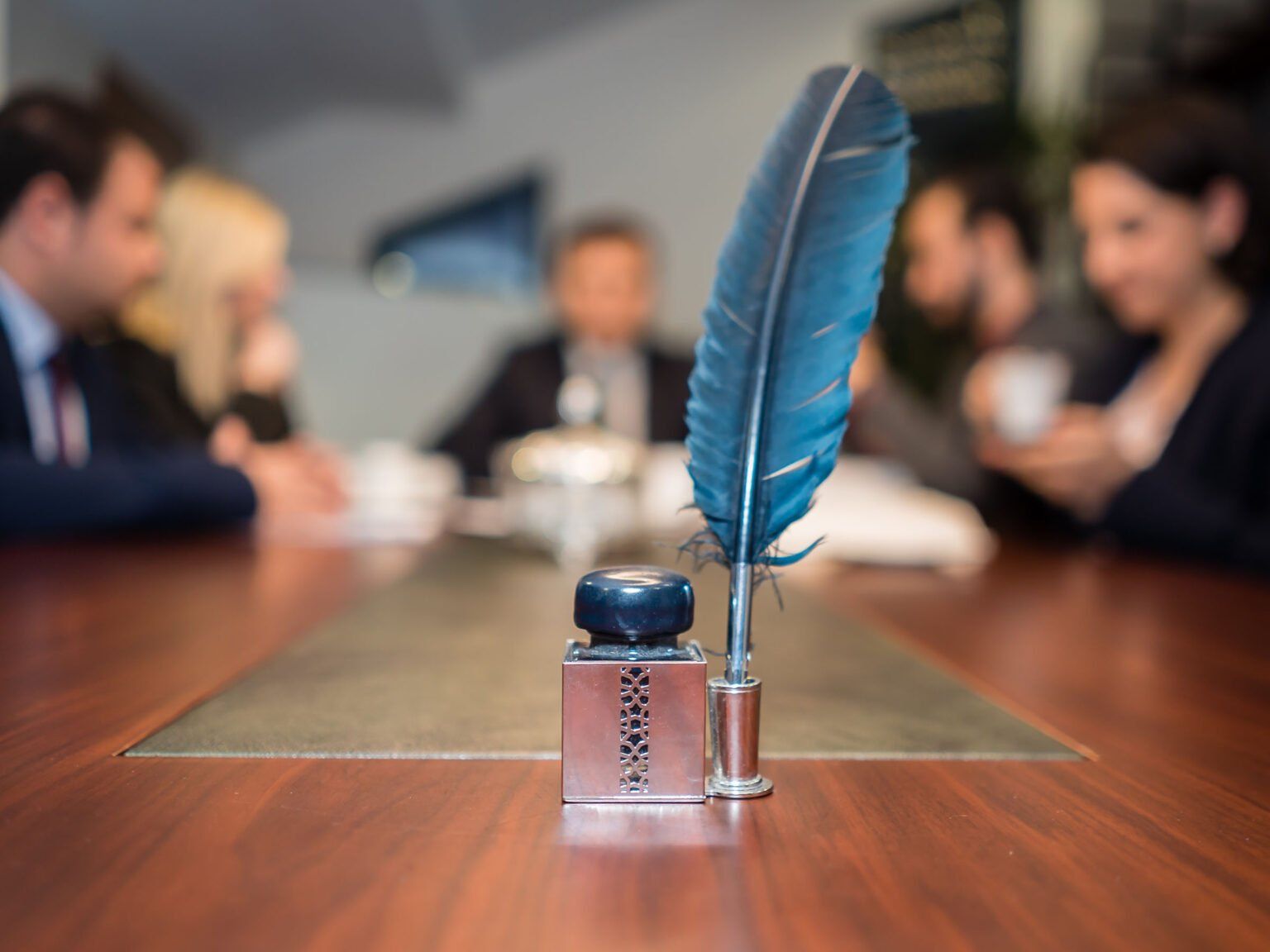 A feather pen is sitting on a wooden table in front of a group of people.