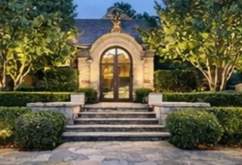 Stone building with arched doorway and steps, framed by hedges and trees, lit at dusk. Stone building with arched doorway and steps, framed by hedges and trees, lit at dusk.