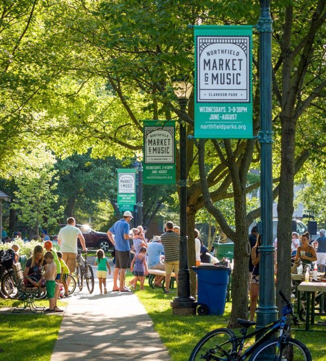 Market and Music event in a park, people gathered near benches, banners on lamp posts. Market and Music event in a park, people gathered near benches, banners on lamp posts.