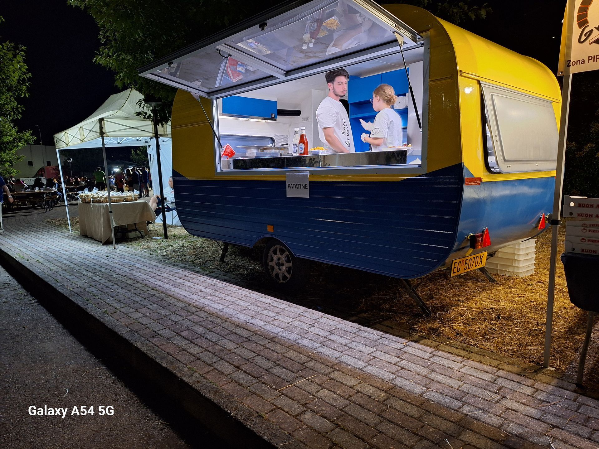 Un camioncino di cibo giallo e blu è parcheggiato sul ciglio della strada di notte.