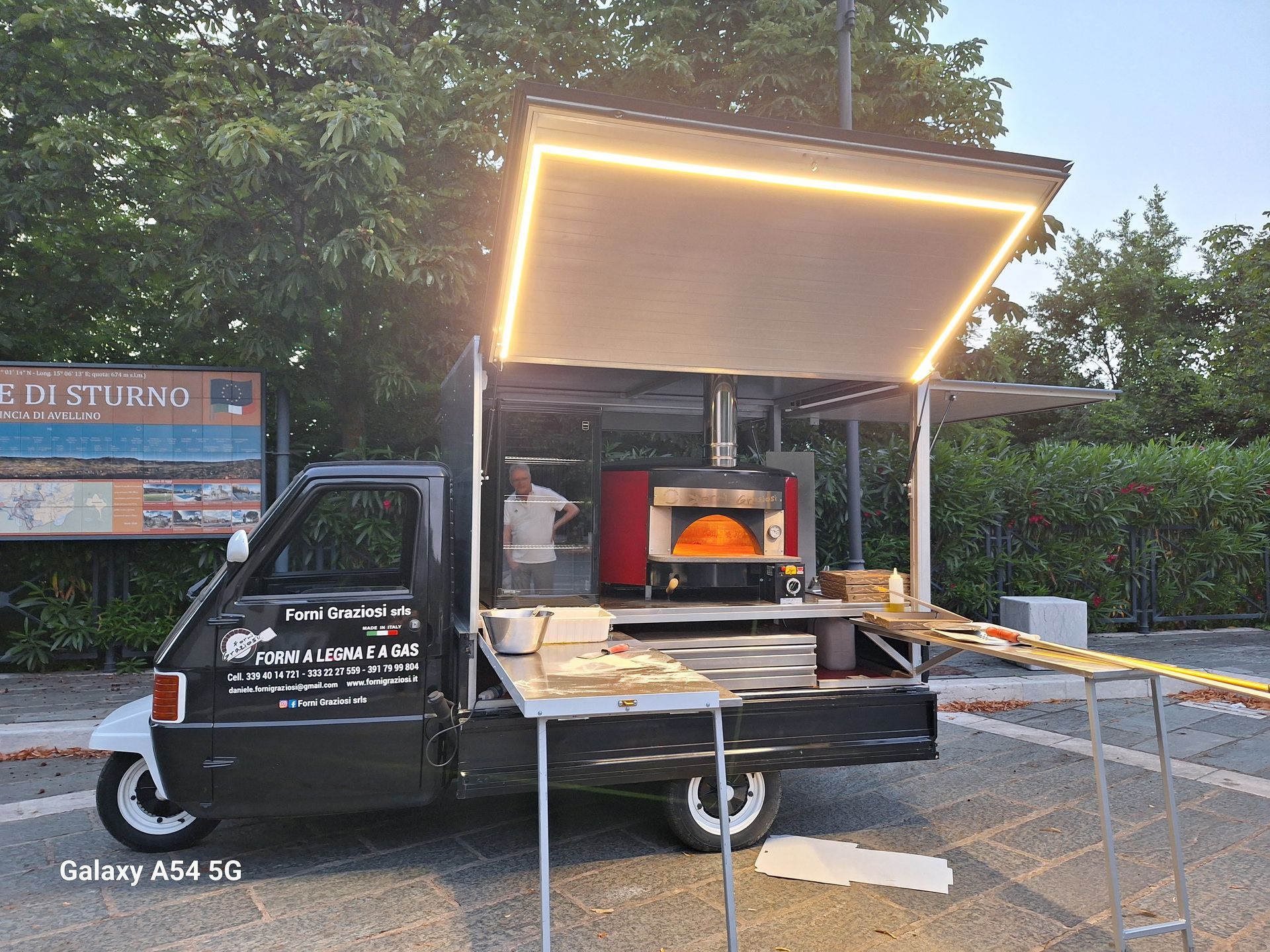 Un camioncino che vende cibo con un forno per pizza sul retro è parcheggiato in un parcheggio.