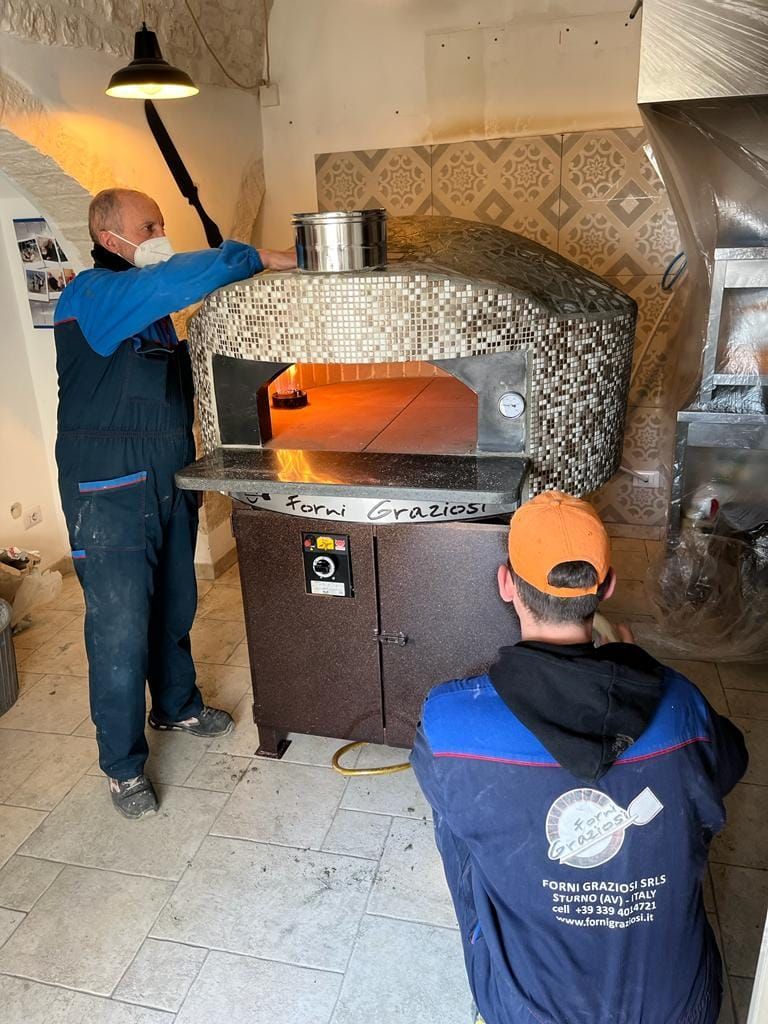 Un uomo che indossa una mascherina è in piedi accanto a un forno per pizza.