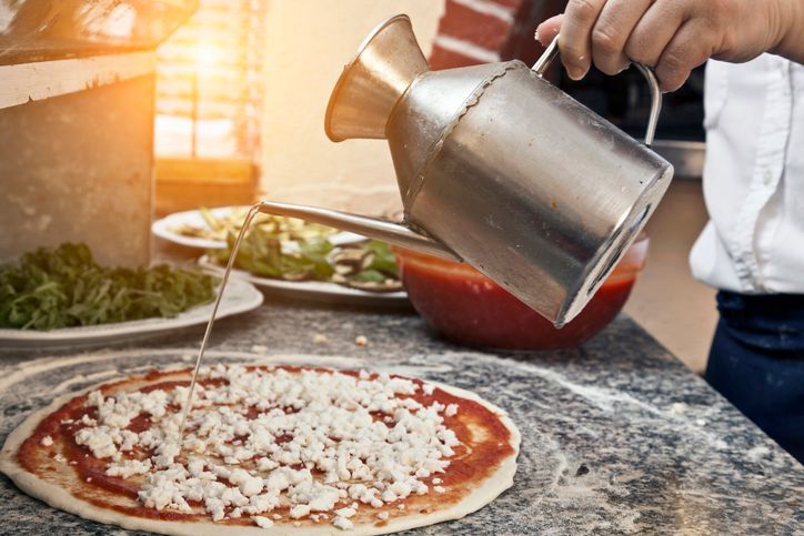 Una persona sta versando dell'olio d'oliva su una pizza.