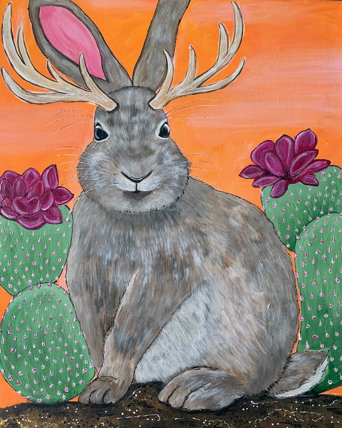 A rabbit with antlers is sitting next to a cactus.