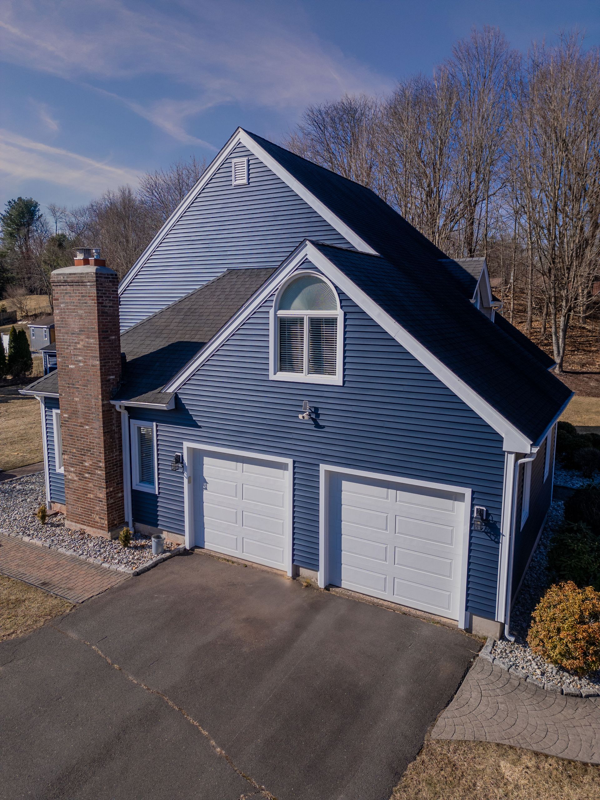 Blue-sided house with white garage doors and a brick chimney. Clear sky, sunny day.