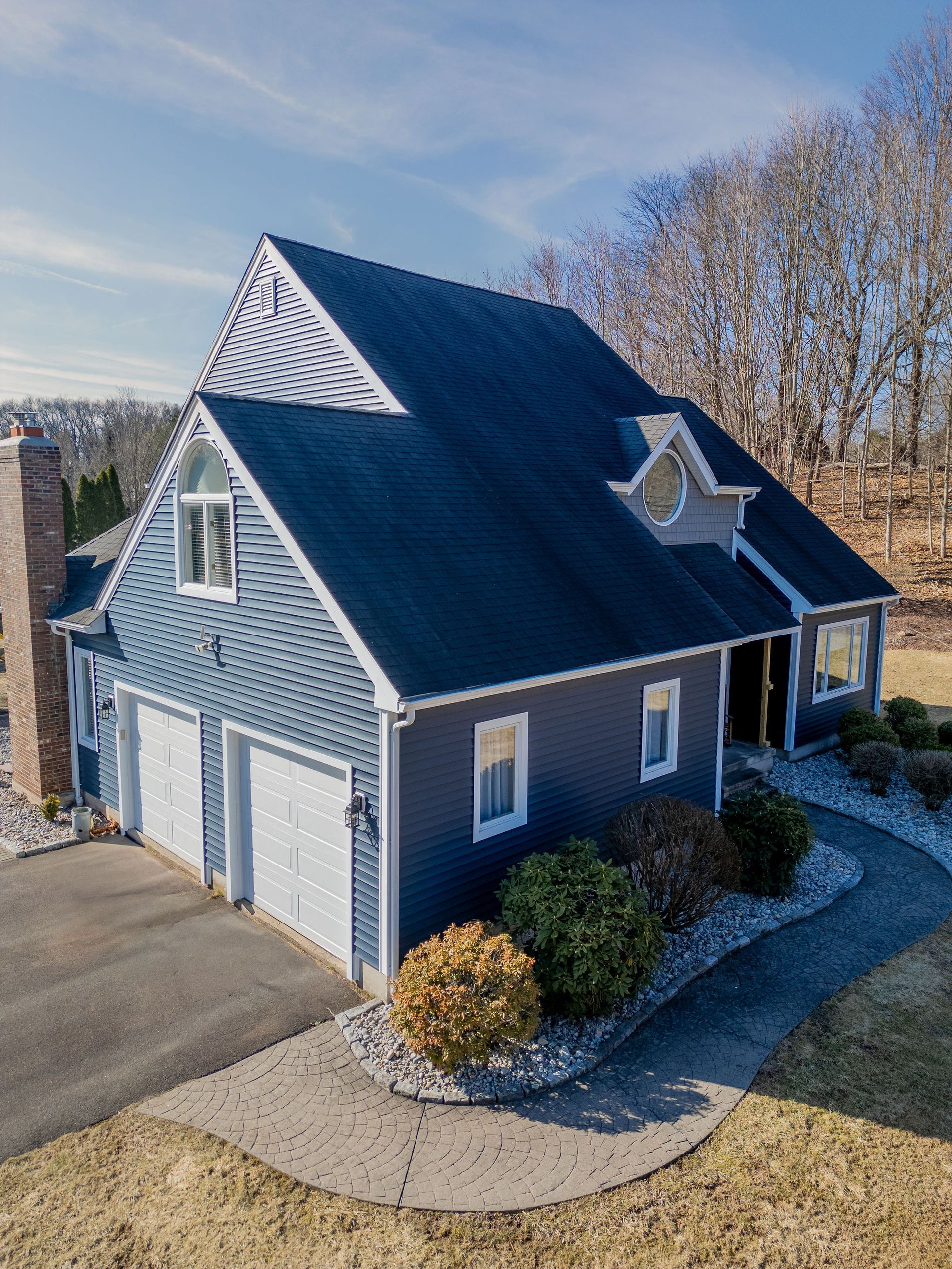 Blue house with a gable roof and a two-car garage, set on a grassy hill on a sunny day.