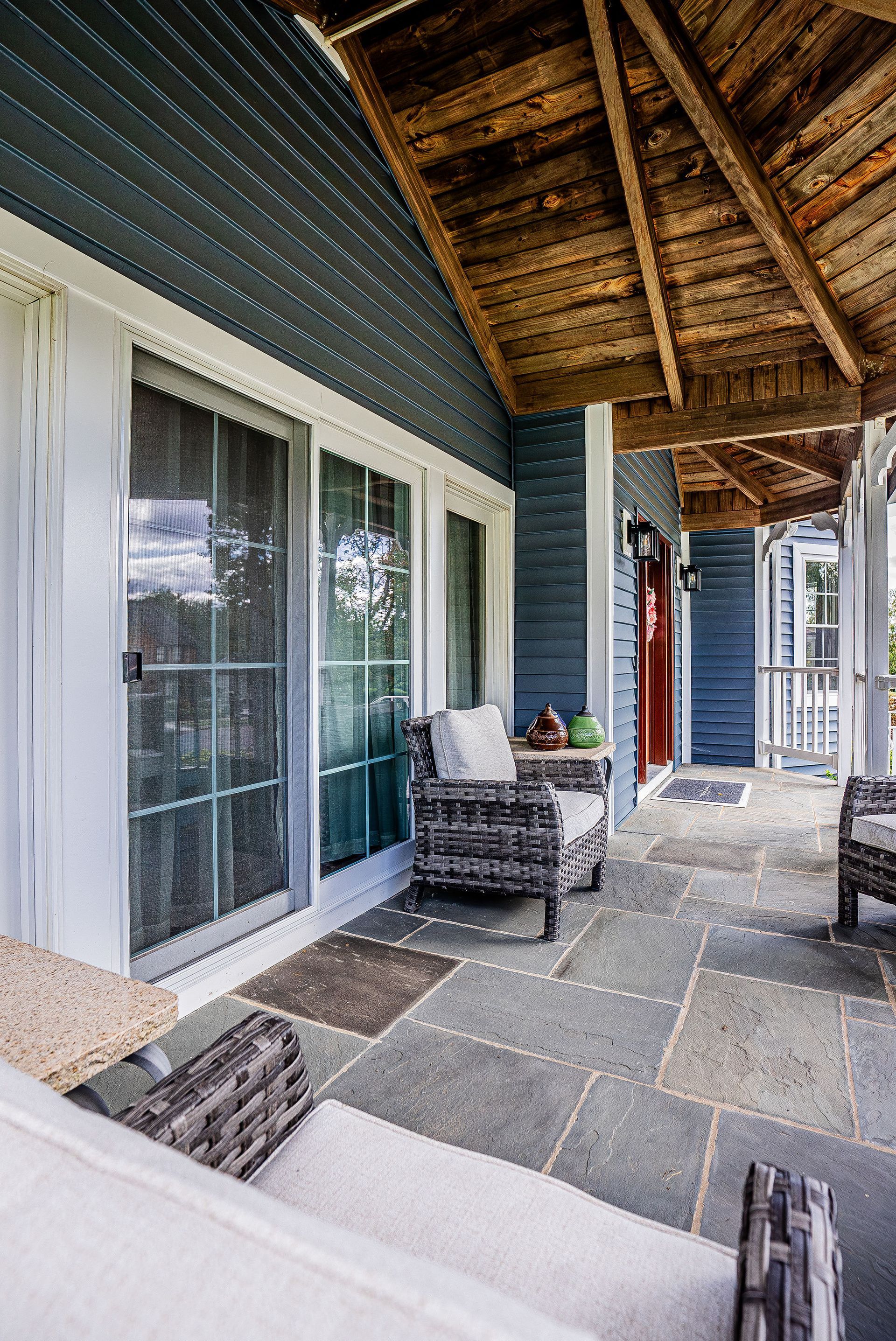 Covered porch with blue siding, stone floor, and wicker furniture.