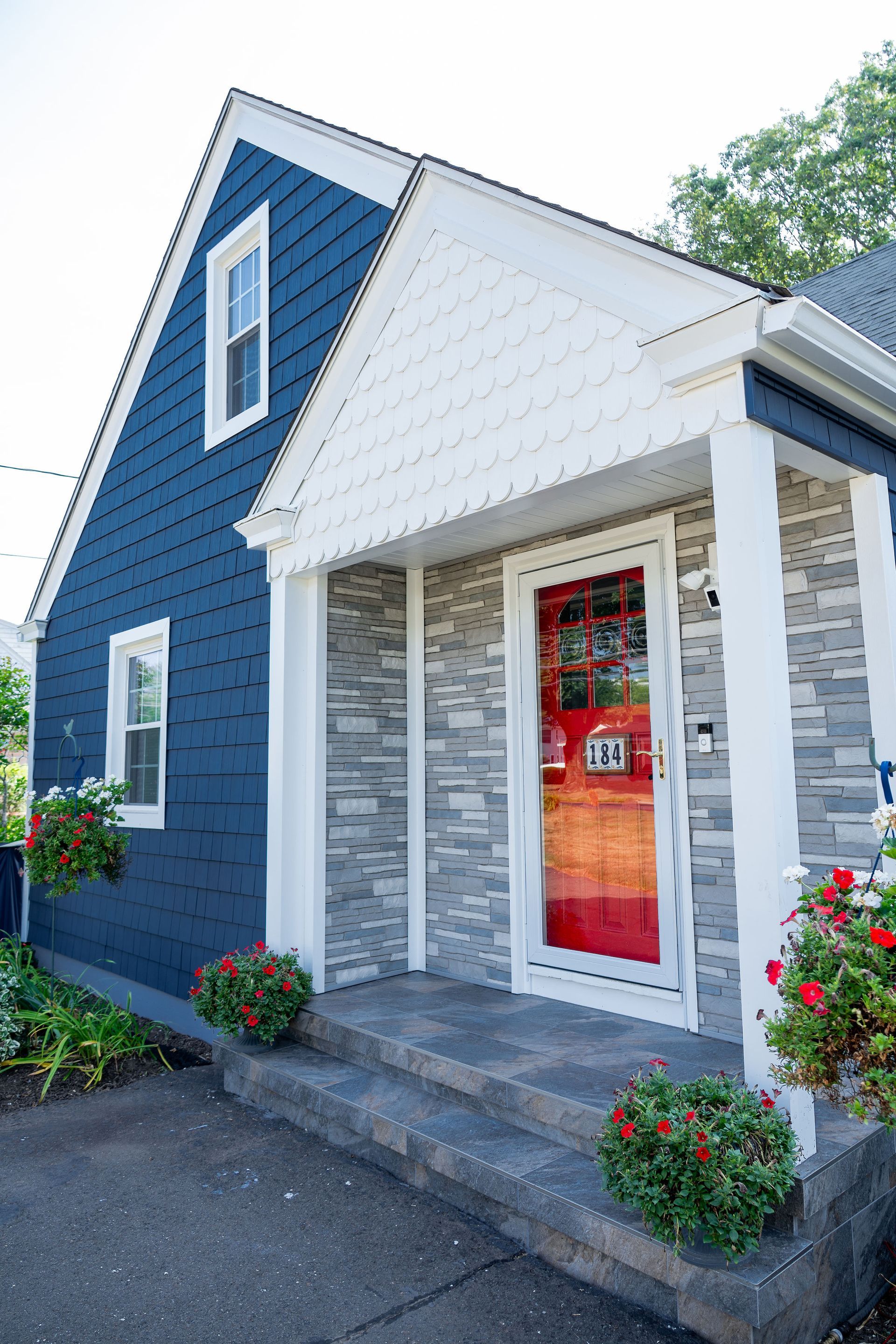 Blue house with white trim, stone entrance, and red door. Flowers decorate the steps.